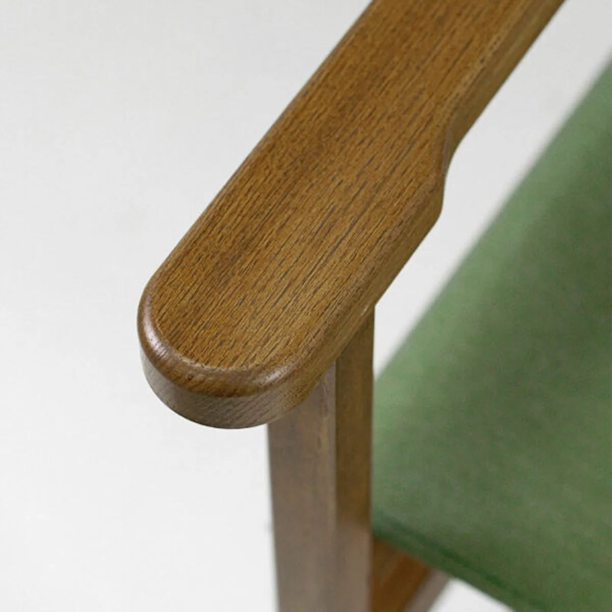 Gros plan sur un accoudoir en bois foncé finition huilée, avec l’assise en toile verte en arrière-plan.