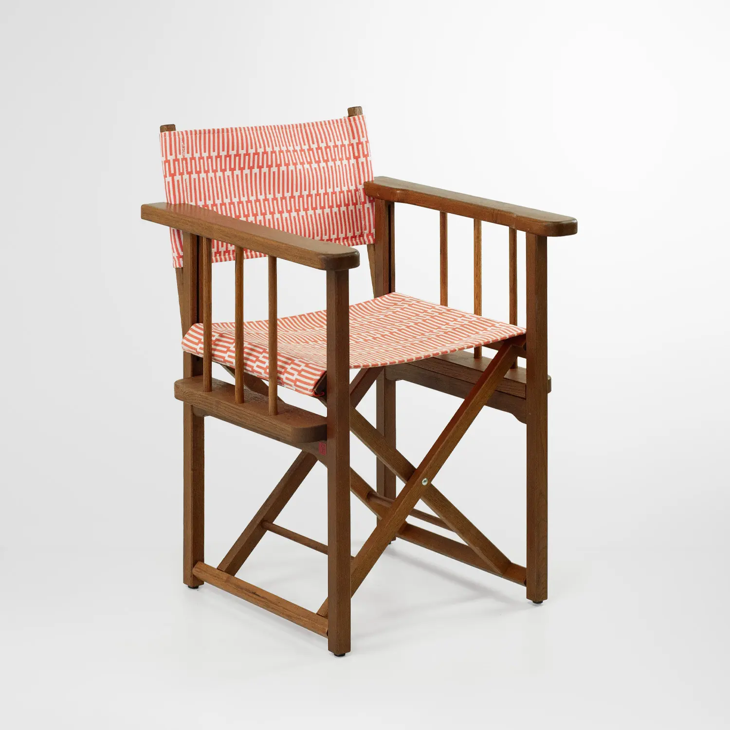 Fauteuil pliant en bois brun, style chaise de réalisateur, avec assise et dossier en toile corail à motif géométrique blanc, sur fond blanc.