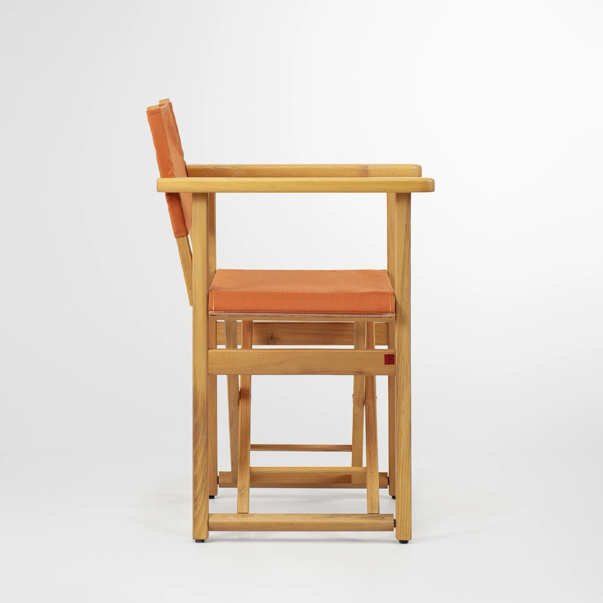 Chaise de metteur en scène en bois clair avec toile orange pour l’assise et le dossier, vue de profil sur fond blanc.