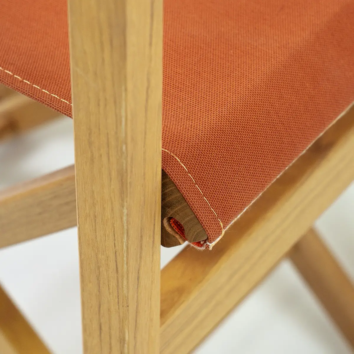 Gros plan sur l’angle de l’assise en toile orange, couture visible et toile enroulée autour d’une barre ronde en bois.