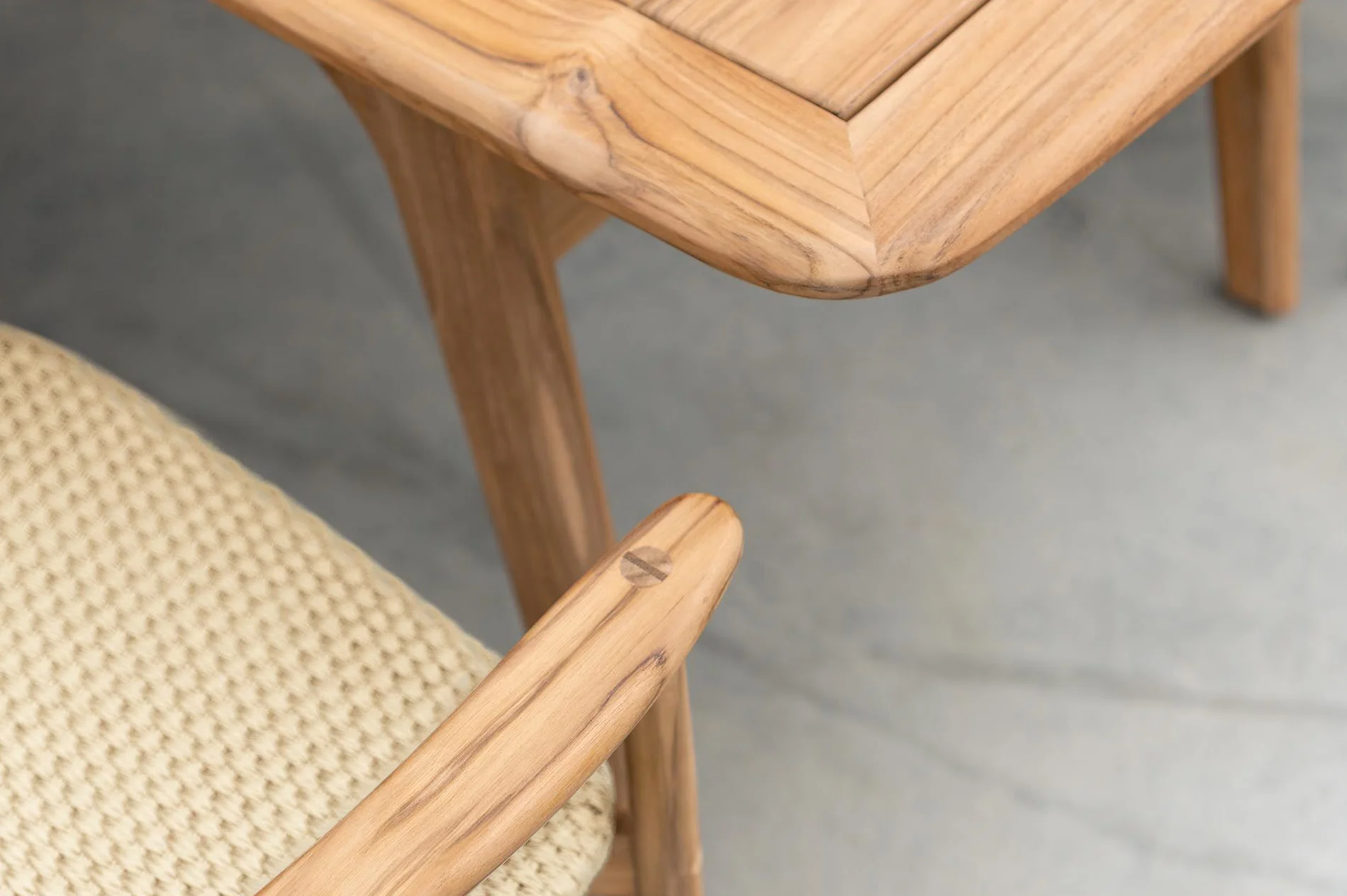 Détail du mobilier de jardin en bois avec plateau de table arrondi, accoudoir et assise tressée.
