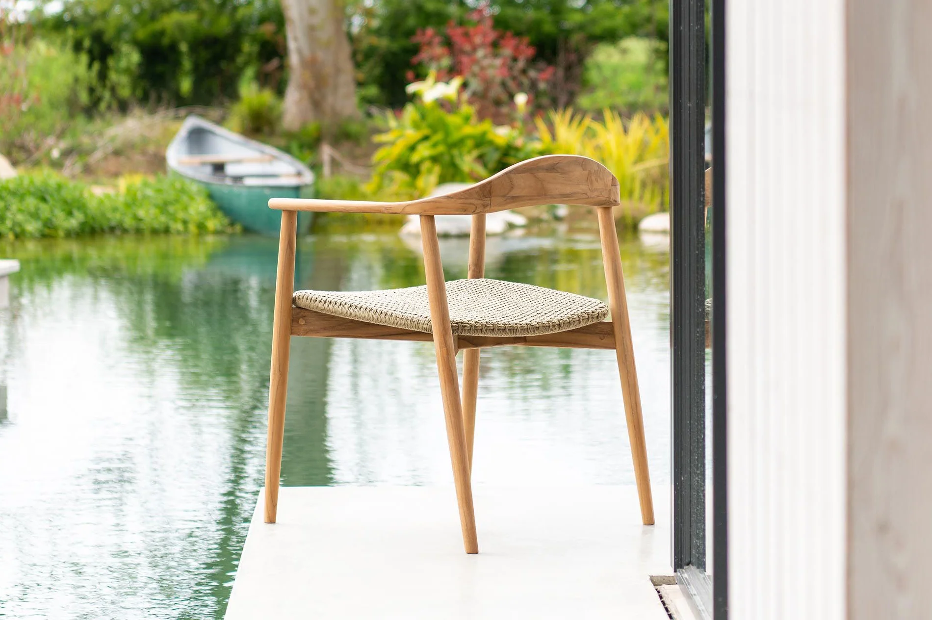 Fauteuil de jardin en bois clair avec assise tressée au bord d’un bassin paysager.